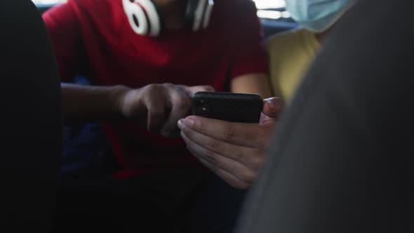 Two mixed race male friends wearing face masks using smartphone in cab