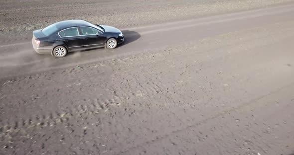 The Car is Racing Along the Road in the Countryside and Blowing a Dusty View From