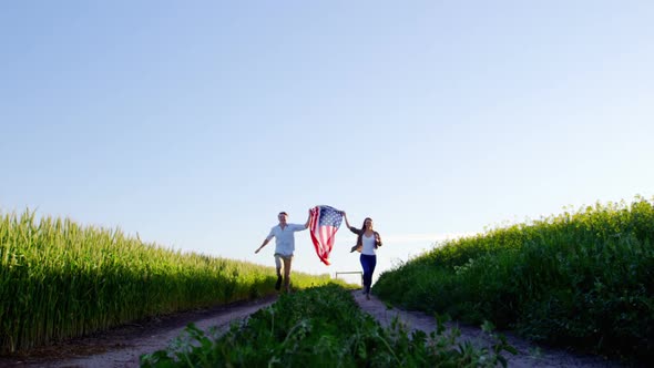 Couple holding american flag and running in field