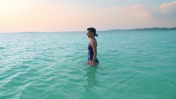 Slow motion: woman swimming in turquoise water sunset sunburst backlight tropica