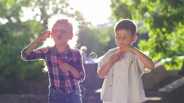 Happy Childhood, Girl and Boy Blowing Soap Bubbles at Park Playing in the Fresh Air in the Backlight