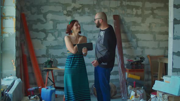 Young excited couple planning their new house renovation looking at blueprints on tablet computer