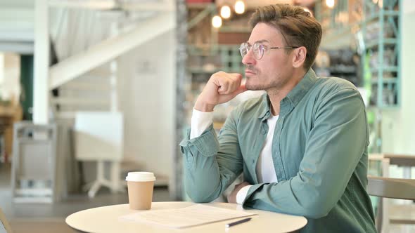 Middle Aged Man Thinking and Reading Documents in Cafe