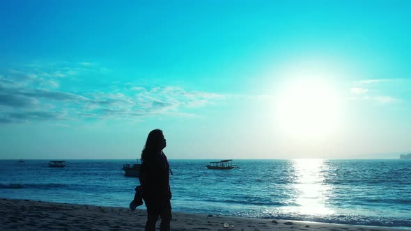 Young woman watching beautiful sunset with glowing sun reflecting on calm sea surface, silhouettes o