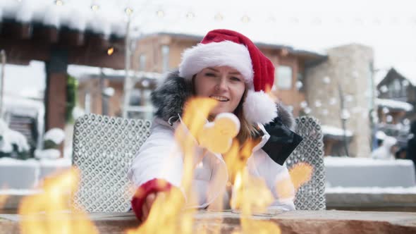 Woman in Red Christmas Hat Roasting Marshmallows in Fire Pit Winter Ski Resort
