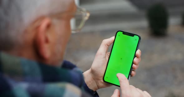 A Warmly Dressed Man Holds a Green Screen Phone