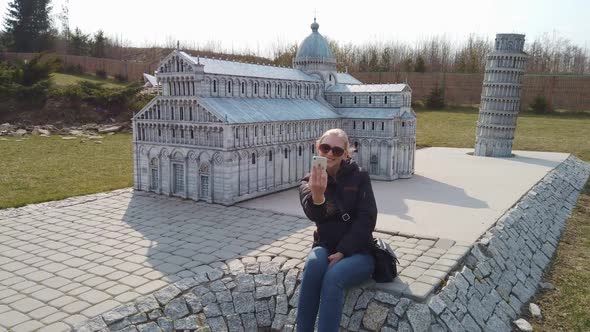 Woman Takes a Selfie Near a Miniature Model of the Old Cathedral, Europe. Park of Miniatures