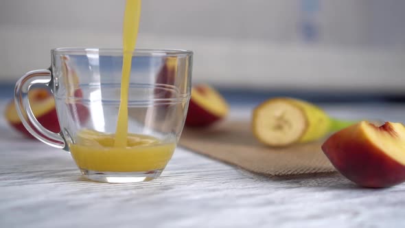 Peach juice is poured into a glass mug on a wooden table with sliced peaches