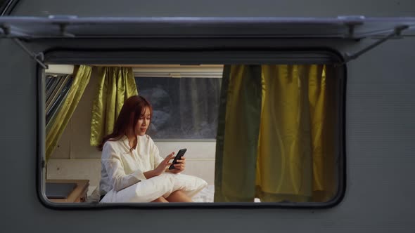 young woman using smartphone on bed of a camper RV van motorhome at night