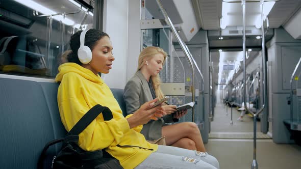 Two Young Girls Sitting in Modern Metro Listening to Music in Headphones
