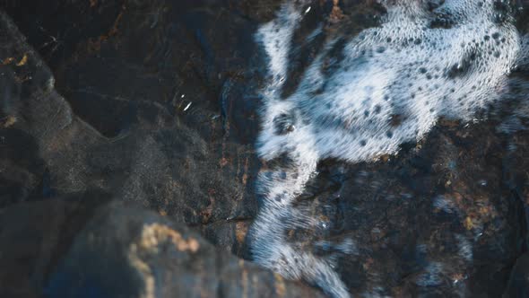 Water waves crashing on black rock and polishing its surface. Coastal erosion