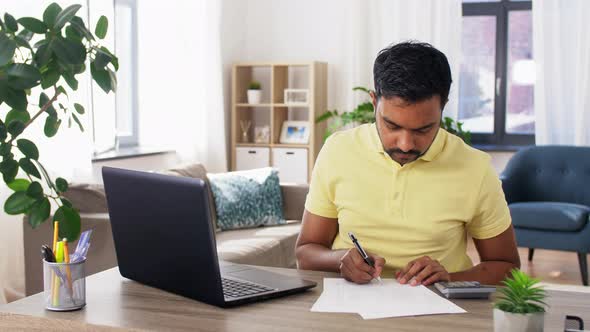 Man with Calculator, Laptop and Papers at Home