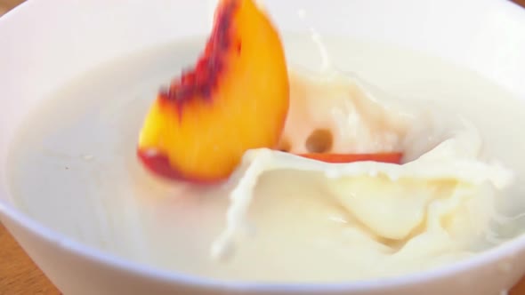 Slices of the Juicy Ripe Peach Are Falling Into the White Bowl with Cream