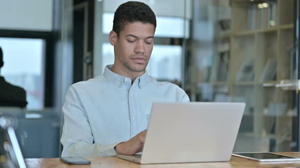 Young African Man Using Laptop in Modern Office