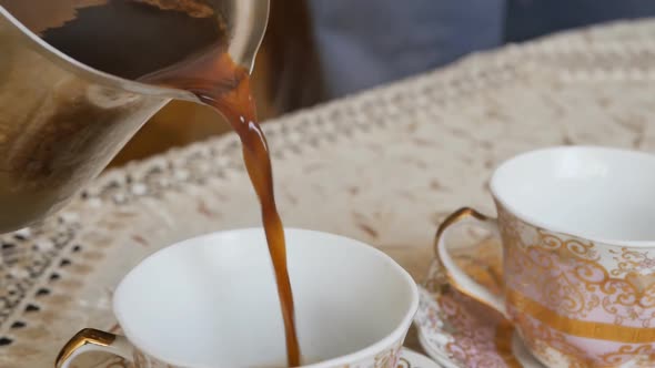 Pour Fresh Hot Natural Coffee Into Two Porcelain Coffee Cups Standing on the Table