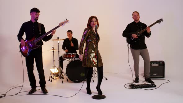 A Mature Musical Band of Four People in Black Clothes Playing Song in the Bright Studio - a Woman