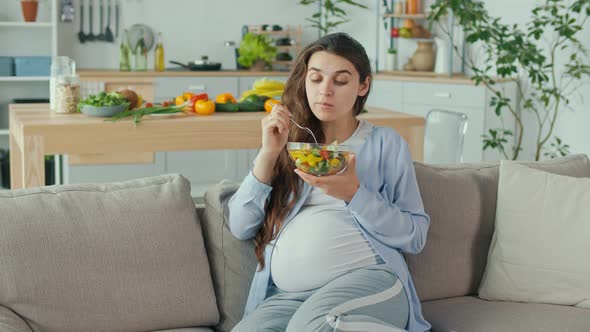 Pregnant Woman With Great Pleasure Eating Vegetable Salad on the Couch