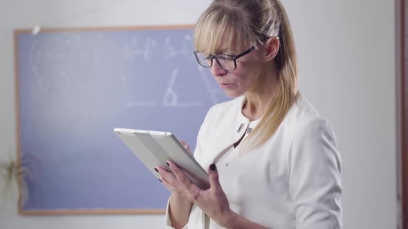 Concentrated Middle Aged Caucasian Woman Standing with Tablet and Looking Back