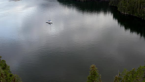 Sailboat Adrift On Calm Lake Surrounded By Lush Trees In Alaska With Cloudy Sky Reflection - aerial