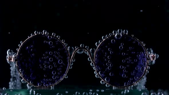 Round Stylish Sunglasses Covered with Air Bubbles in Transparent Water on a Black Background