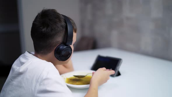 Boy with tablet in the kitchen. Boy eating his lunch and enjoy watching his tablet