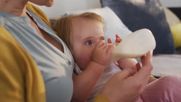 Mid section of caucasian mother feeding milk to her baby in the bed at home