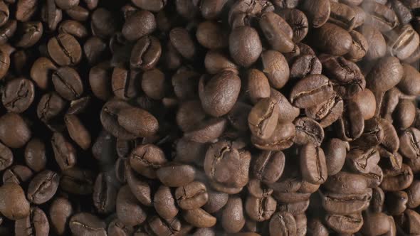 Close up top down shot of brown coffee beans on a roasting pan, light smoke being released as the be