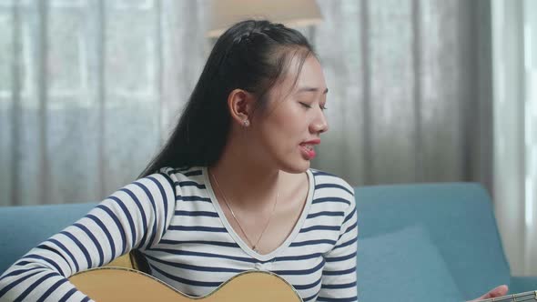 Asian Woman Singing And Playing A Guitar At Home