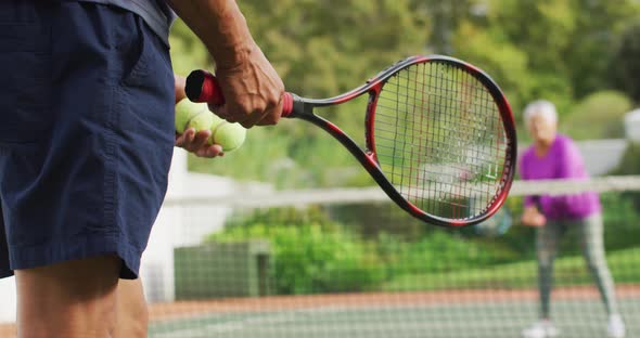 Video of hands of biracial senior man holding racket and starting match on tennis court