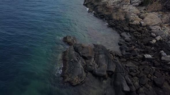 Aerial: A slow forward flight over the rocky shore and big stones revealing the horizon, island and