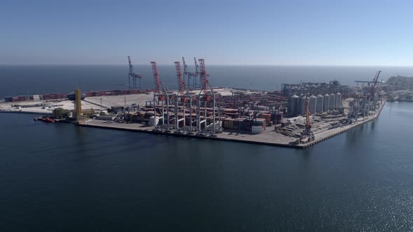 Commercial Port with Container and Lifting Cranes on Sea Waterfront Against Blue Sky and Shiny Water