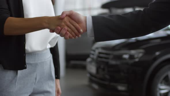 Salesman Shaking Hands with Man and Woman in Car Showroom