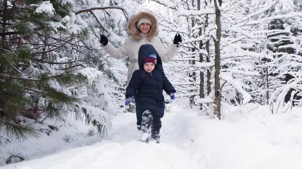 Mom and Son are Running in a Snowy Winter Forest Happy Parenthood and Family Vacation Slow Motion