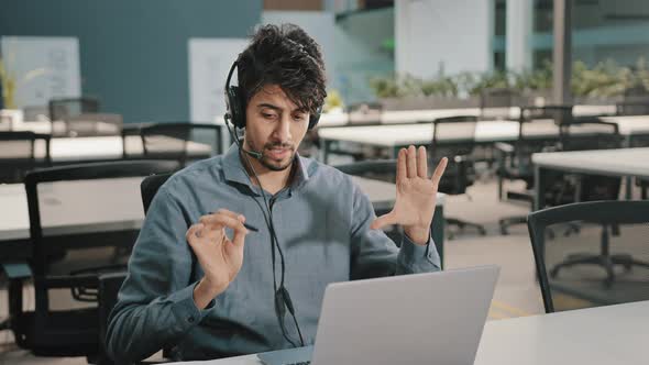 Young Indian Businessman Investor Wearing Headphones Communicate By Video Call Conference on Laptop