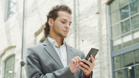 A young successful businessman is working outdoor using smartphone.