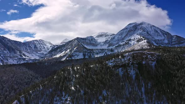 Cloud blowing over snow capped mountain towering over forest