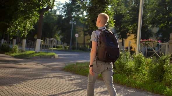 Back-side View of Student Photographer with a Black Backpack Is Walking Along a Town Street