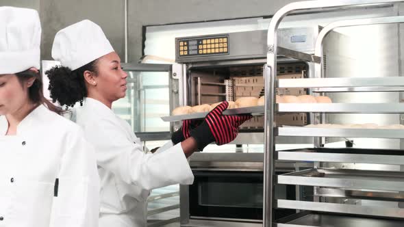 Female chef in uniform prepare to bake bread and pastry in stainless kitchen.