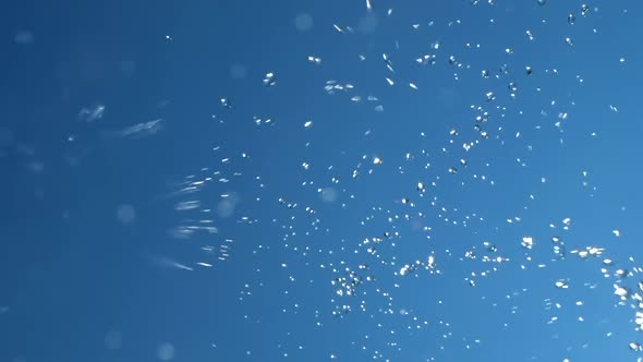 Flying Drops and Splashes of Water on Background of Blue Sky and Bright Sun. Concept of Cleanliness