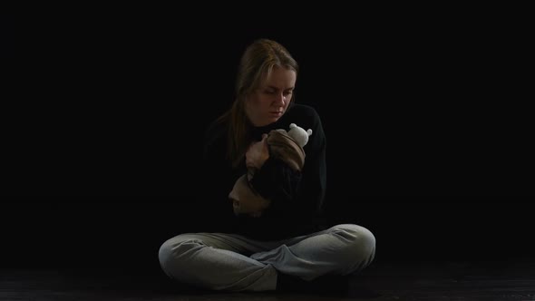 Depressed Lady Sitting in Darkness Hugging Teddy Bear, Obstetric Violence Victim