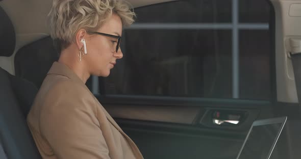 Side View of Stylish Business Woman Working on Laptop While Sitting on Back Seat of a Car