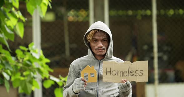 Homeless man holding homeless label, home paper and looking at camera.