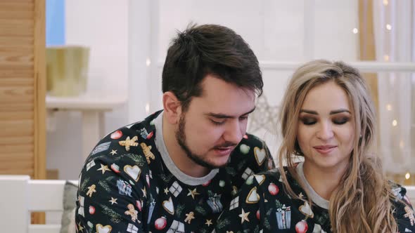 Attractive Cheerful Man and Woman Sitting Near Christmas Tree Hugging