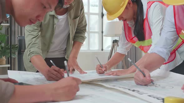 Three Asian Engineers With Helmets Helping A Man Drawing Building Construction At The Office