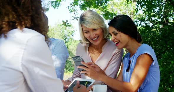 Female friends discussing over mobile phone at outdoor cafe