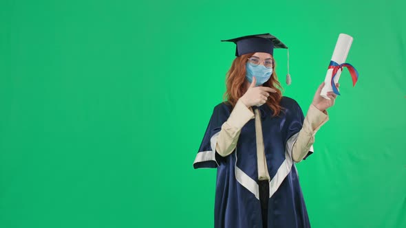 Female Graduate in Academic Hat and Mantle in Medical Mask on Face Points to Diploma Then Finger Up