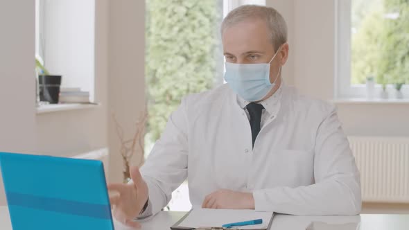 Middle Shot of Professional Male Physician in Face Mask Consulting Patient Online in Virtual