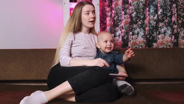 A Young Mother and Her Young Son Sit on the Couch and Look at Pictures on Their Phone