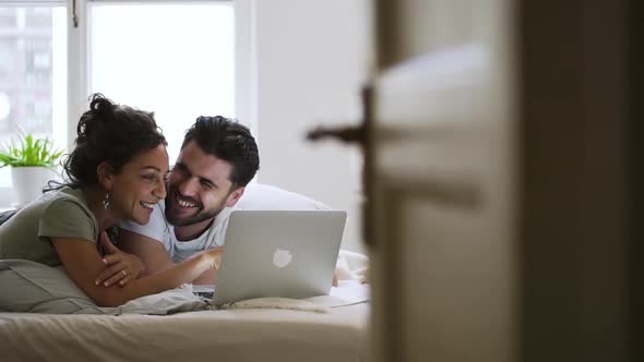 Beautiful American Couple is Lying on Bed and Using Laptop in Modern Apartment Spbd