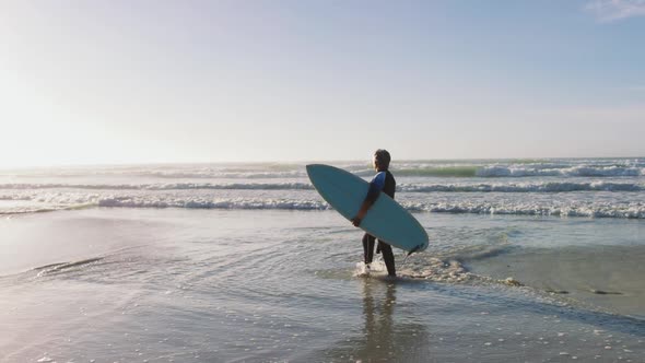 Senior african american woman walking with a surfboard at the beach